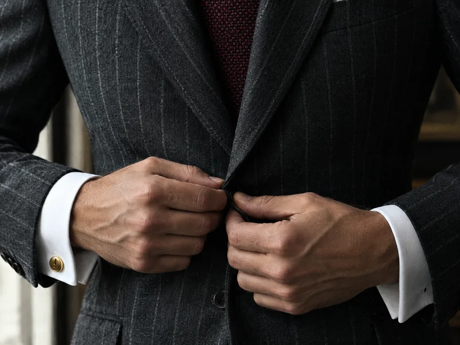 Hands fastening the button of a charcoal chalk-stripe jacket